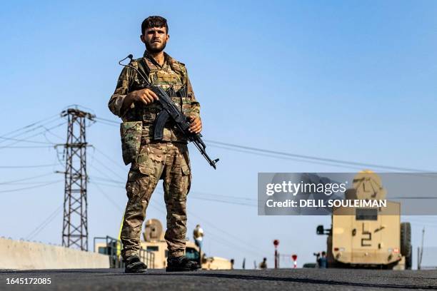 Fighter of the Syrian Democratic Forces stands guard along a road as others deploy to impose a curfew in the town of al-Busayrah in Syria's...