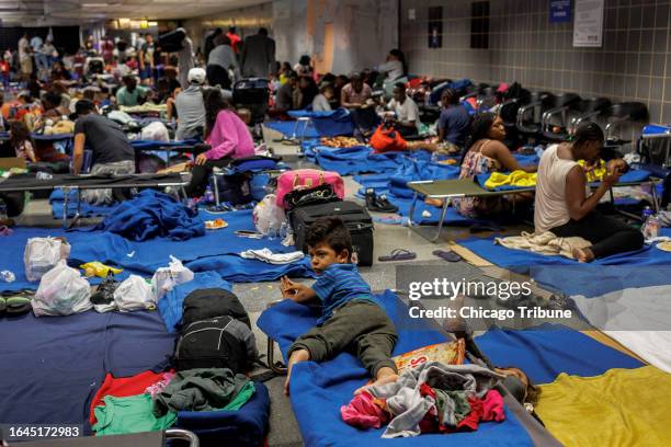 Recently arrived migrants sit on cots and the floor of a makeshift shelter operated by the city at O'Hare International Airport on Aug. 31, 2023.