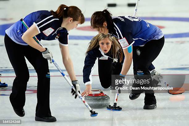 Eve Muirhead of Scotland throws the stone as team mates as Vicki Adams and Claire Hamilton sweep during the Gold medal match between Sweden and...