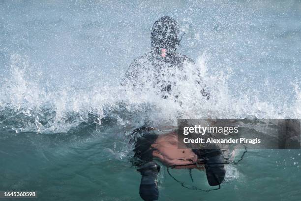 rear view of a surfer athlete riding a breaking wave of the pacific ocean lying on front on surfboard. view of the surfer half above the water and underwater - woman lying on stomach with feet up stock pictures, royalty-free photos & images