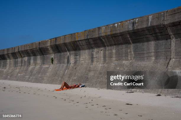 Woman relaxes on the beach next to Longis anti-tank wall, a 6-meter high concrete wall built by forced labour under German forces to prevent an...