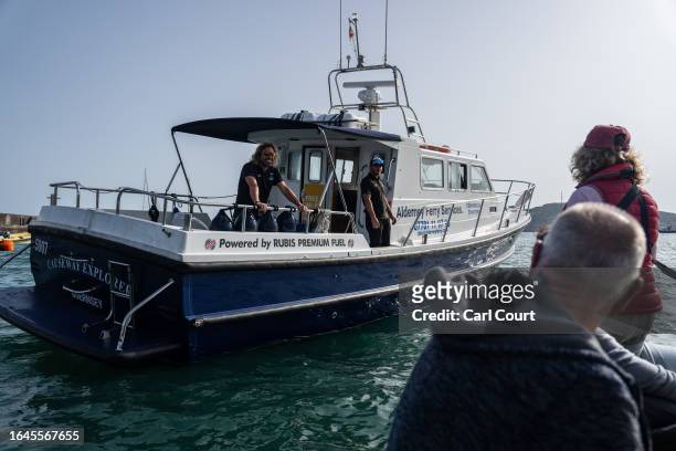 Crew members welcome passengers as they arrive by dinghy to board the Alderney to Guernsey ferry on September 5, 2023 in Alderney, Guernsey. This...