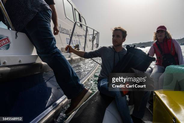 Passengers cross from a dinghy to board the Alderney to Guernsey ferry on September 5, 2023 in Alderney, Guernsey. This year, the British government...