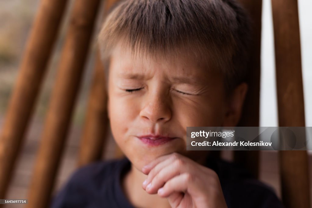 Boy 8 years old squinting while sitting in wooden chair