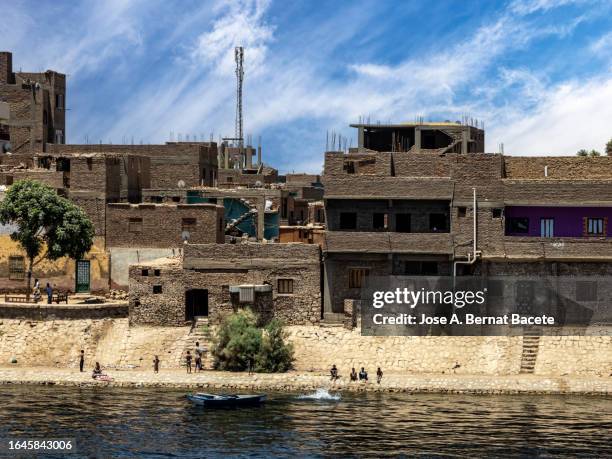 small town with a group of children playing and bathing on the bank of the nile river in egypt. - nile river stock pictures, royalty-free photos & images