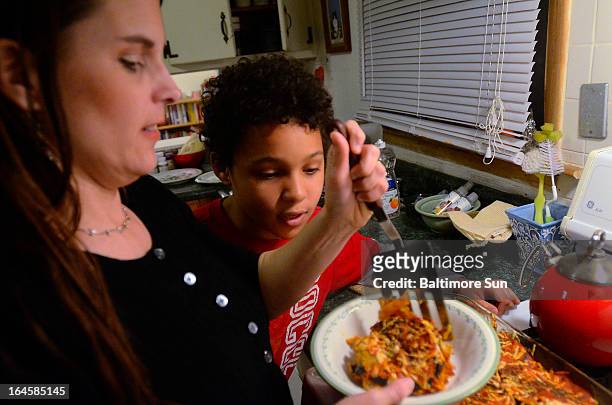 Tyler watches his mother Lesley Parker-Rollins, left, dish out his dinner bowl at their Lutherville-Timonium, Maryland home, March 7, 2013.