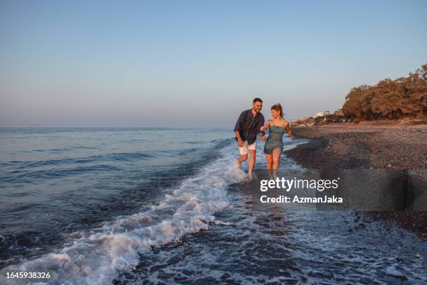 a cute young caucasian couple chasing each other during their date on the beach - golden hour beach stock pictures, royalty-free photos & images