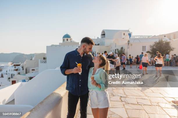a caucasian young adult tourist couple in love walking around santorini eating ice cream - honeymoon stock pictures, royalty-free photos & images
