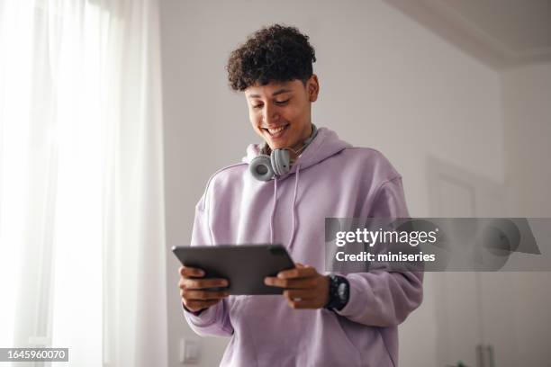 portrait of a smiling teenage boy standing and using a digital tablet - man holding headphones stock pictures, royalty-free photos & images