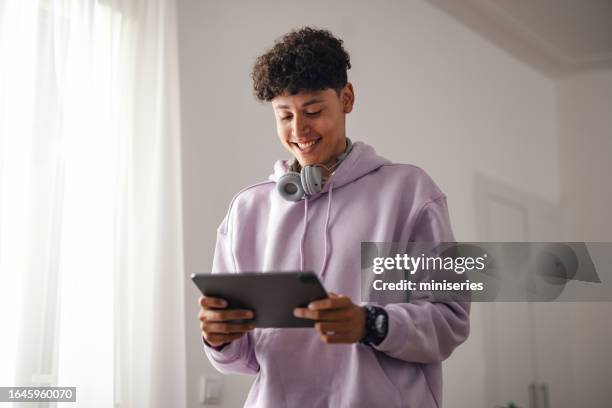 portrait of a smiling teenage boy standing and using a digital tablet - holding tablet computer stock pictures, royalty-free photos & images