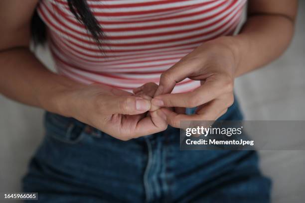 woman sitting on sofa, suffering from skin picking disorder, touching fingernails, feeling stressed and anxious. anxiety and mental health - fingernagel stock-fotos und bilder