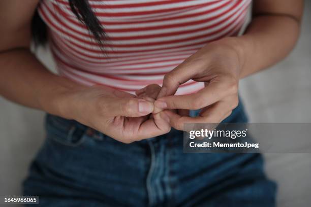 woman sitting on sofa, suffering from skin picking disorder, touching fingernails, feeling stressed and anxious. anxiety and mental health - neuropathy stockfoto's en -beelden