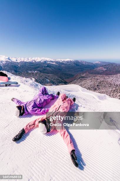 two female snowboarder relax lying down on the edge of the ski slope - vacaciones en la nieve fotografías e imágenes de stock