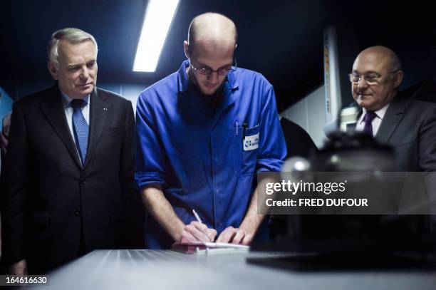 French Prime Minister Jean-Marc Ayrault and French Labour, Employment and Social Dialogue Minister, Michel Sapin stand beside a young man signing a...