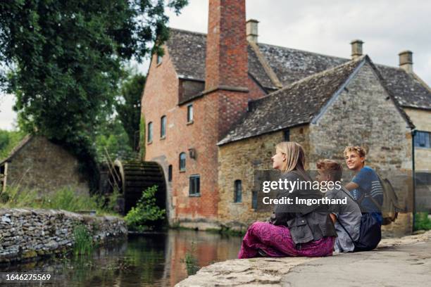 three teenagers walking in beautiful village of lower slaughter on a warm summer evening - cotswolds stock pictures, royalty-free photos & images