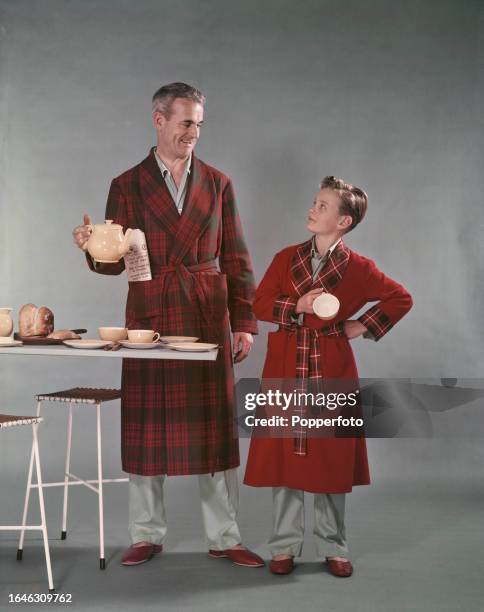 Posed studio portrait of a father and son wearing tartan and red wool dressing gowns over matching pyjamas and slippers, the boy holds a cup and the...