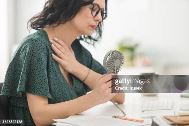 reife frau leidet unter hitzewallung im büro - menopause stock-fotos und bilder