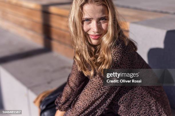 portrait of smiling young woman sitting on steps in sunlight - tossing hair facing camera woman outdoors stock pictures, royalty-free photos & images