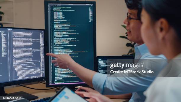 closeup group of asian people software developers using computer to write code sitting at desk with multiple screens in office at night. programmer development. - datawetenschapper stockfoto's en -beelden