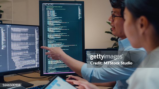 Closeup group of Asian people software developers using computer to write code sitting at desk with multiple screens in office at night. Programmer development. Closeup group of Asian people software developers using computer to write code sitting at desk with multiple screens in office at night. Programmer development.