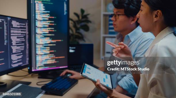 gruppo di sviluppatori di software di persone asiatiche che utilizzano il computer per scrivere codice seduti alla scrivania con più schermi in ufficio di notte. sviluppo programmatore. - programmazione televisiva foto e immagini stock