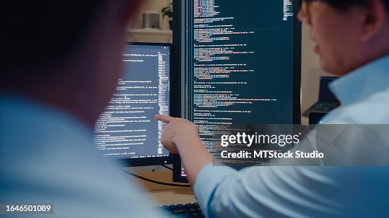 Closeup group of Asian people software developers using computer to write code sitting at desk with multiple screens in office at night. Programmer development. Closeup group of Asian people software developers using computer to write code sitting at desk with multiple screens in office at night. Programmer development.