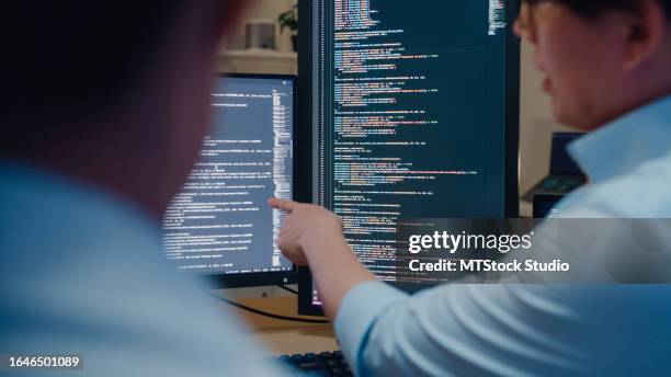 closeup group of asian people software developers using computer to write code sitting at desk with multiple screens in office at night. programmer development. - computersoftware stockfoto's en -beelden