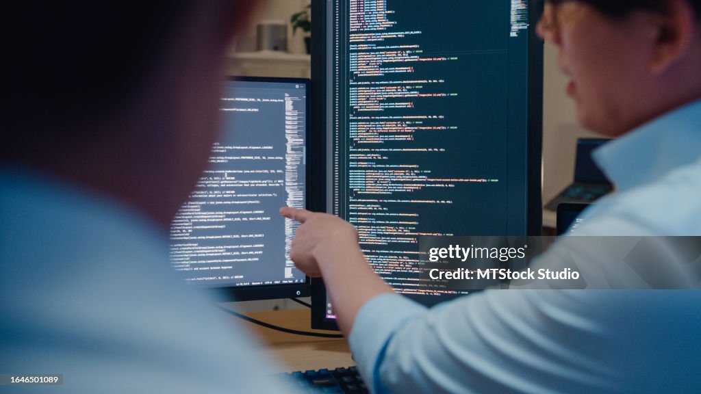 Closeup grupo de pessoas asiáticas desenvolvedores de software usando o computador para escrever código sentado na mesa com várias telas no escritório à noite. Desenvolvimento de programadores.
