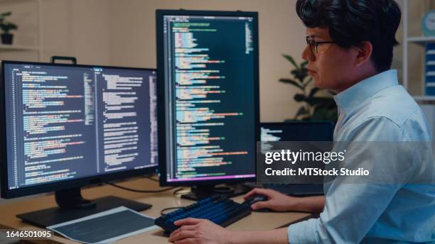i giovani sviluppatori di software asiatici che usano il computer per scrivere codice seduti alla scrivania con più schermi lavorano in ufficio di notte. sviluppo programmatore. - programmazione televisiva foto e immagini stock