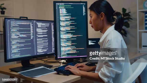 young asian woman software developers using computer to write code sitting at desk with multiple screens work in office at night. programmer development. - javascript stock pictures, royalty-free photos & images