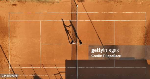 zwei tennisspieler schütteln sich in der mitte des platzes die hände - tennisnetz stock-fotos und bilder