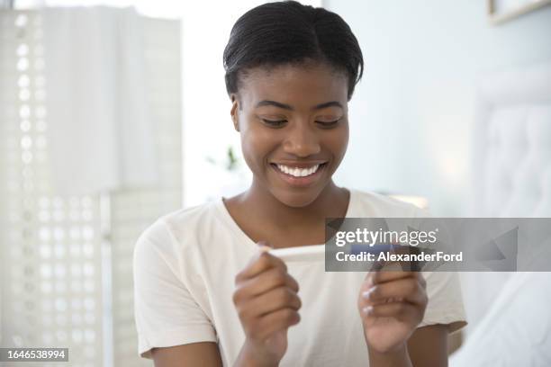 pregnancy test, happy and black woman on a bed with positive results, smile and excited in house. pregnant, testing and african female in bedroom with home kit for ivf or fertility treatment success - in vitro fertilization stock pictures, royalty-free photos & images