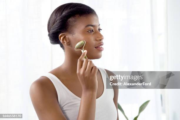 black woman, jade roller and massage face for beauty, detox dermatology or aesthetic wellness. female person, crystal stone tools and facial skincare for lymphatic drainage, glow and collagen at home - verde jade imagens e fotografias de stock