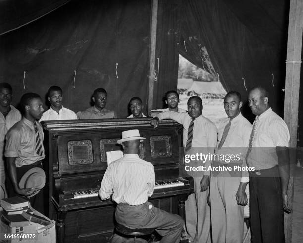 Jamaican farm workers gather around the piano to sing hymns in the recreation tent at a Farm Security Administration camp, United States, circa 1940....