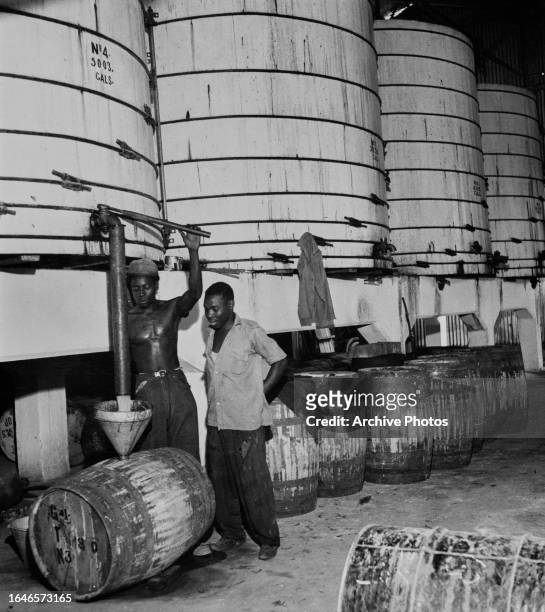 Distillery workers using a funnel to fill a barrel with rum from a large vat at a distillery in Jamaica, circa 1945.