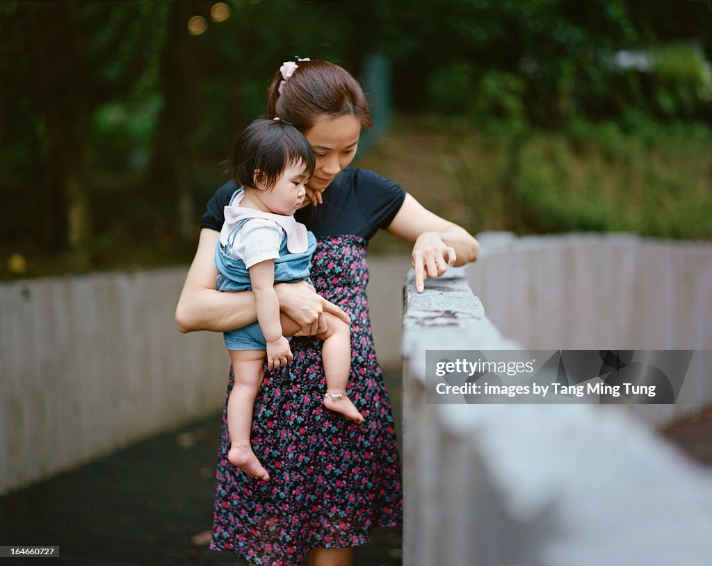 Mom holding baby showing her something in park