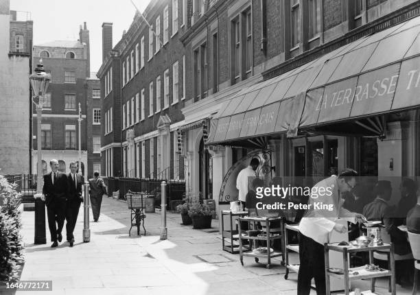 Waiter and food trolley outside a restaurant at Shepherd Market while pedestrians walk by, Mayfair, London, July 1964.