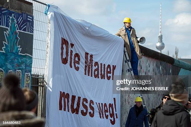 German comedian Tobias Schlegl takes part on an action next to a banner "Die Mauer muss weg" at the East Side Gallery part of the remains of the...