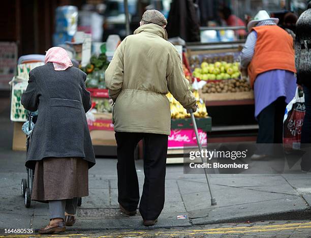 An elderly man and woman make their way past market stalls in Moore Street in Dublin, Ireland, on Saturday, March 16, 2013. Ireland’s renewed...