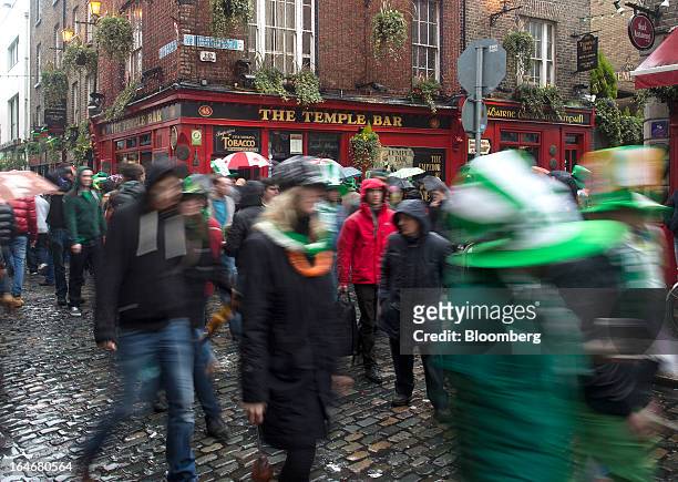 Pedestrians carrying umbrellas and wearing St. Patrick's day hats and scarves move past the Temple Bar public house in Dublin, Ireland, on Sunday,...