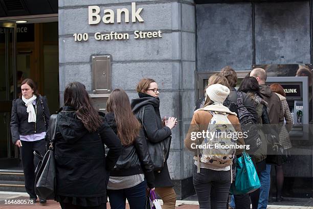 Customers line up to use an automated teller machine outside a branch of the Allied Irish Bank on Grafton Street in Dublin, Ireland, on Thursday,...