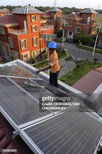 An Indian worker cleans solar panels fitted onto the roof of a residential house in Rabirashmi Abasan, a solar housing complex at Rajarhat close to...