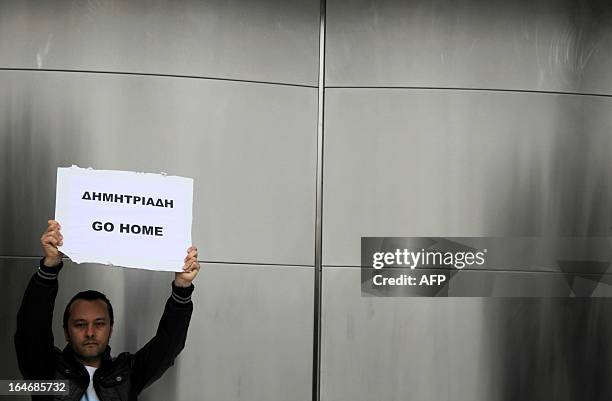 An employee of the Central Bank of Cyprus holds a sign reading in Greek: "Demitriades go home" referring to the bank's governor, during a...