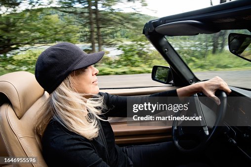 Beautiful mature woman driving convertible car in country.