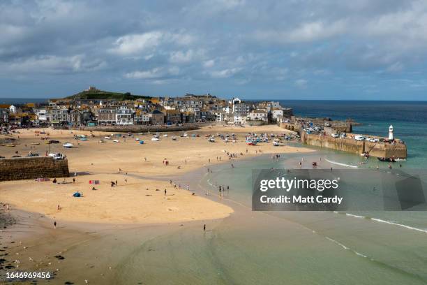 People gather on the beach at low tide at the harbour at St Ives on August 21, 2023 in Cornwall, England.