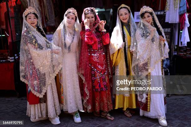 This photo taken on July 13, 2023 shows women wearing traditional Uyghur attire posing for a photo at the Old Kashgar tourist area in China's...