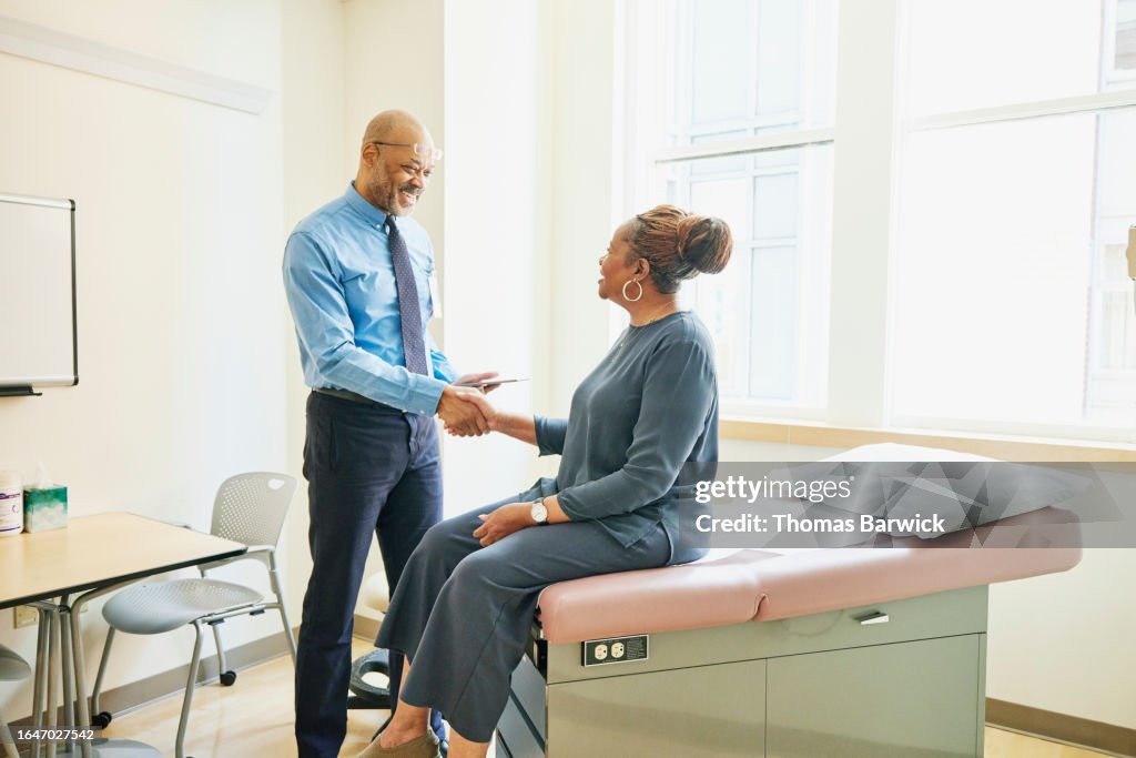 Wide shot doctor shaking hands with senior female patient in exam room