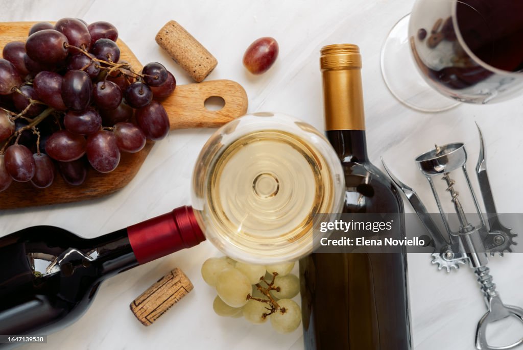 Glass of white wine and bottles of red and white wine and fresh grapes