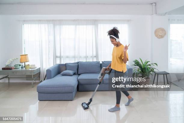 young woman with wireless headphones using vacuum cleaner for cleaning her house. - aspirapolvere foto e immagini stock