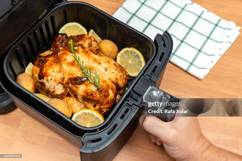 HAND COOKING WHOLE ROASTED CHICKEN WITH GARNISH IN AIR FRYER AT THE KITCHEN. TOP VIEW.
